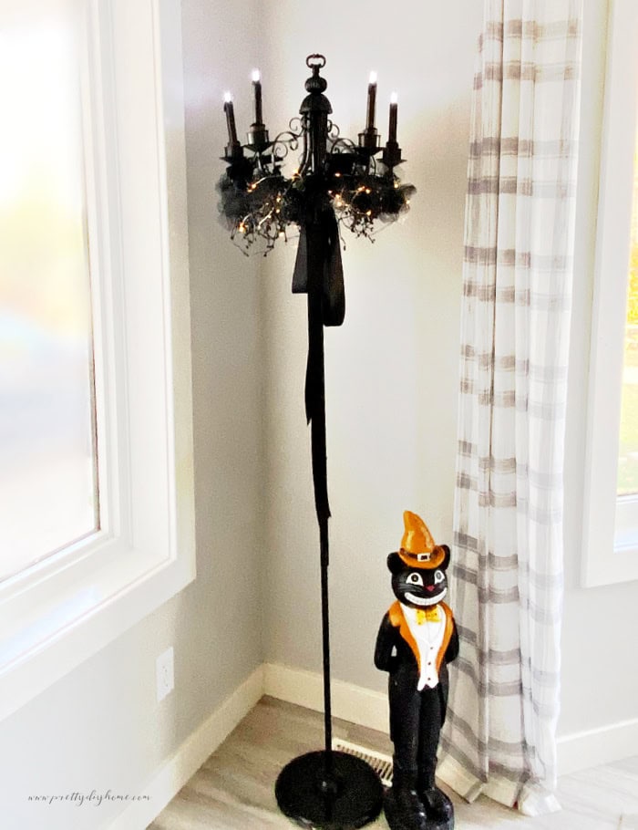 A scary DIY Halloween chandelier in all black with a gothic look.  There is a fancy black cat butler decoration standing at the bottom.