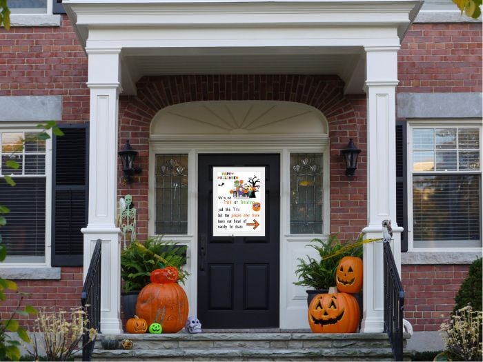 An Halloween porch decorated with a free printable Halloween candy sign, and flanked with two large jack-o-lanterns on each side of the black door.