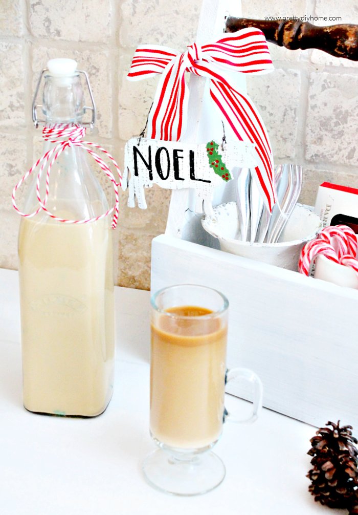 A bottle of homemade Bailey's in a tall bottle and a cup of coffee in a tall clear cup where you can see the layers of Baileys Irish Cream inside.