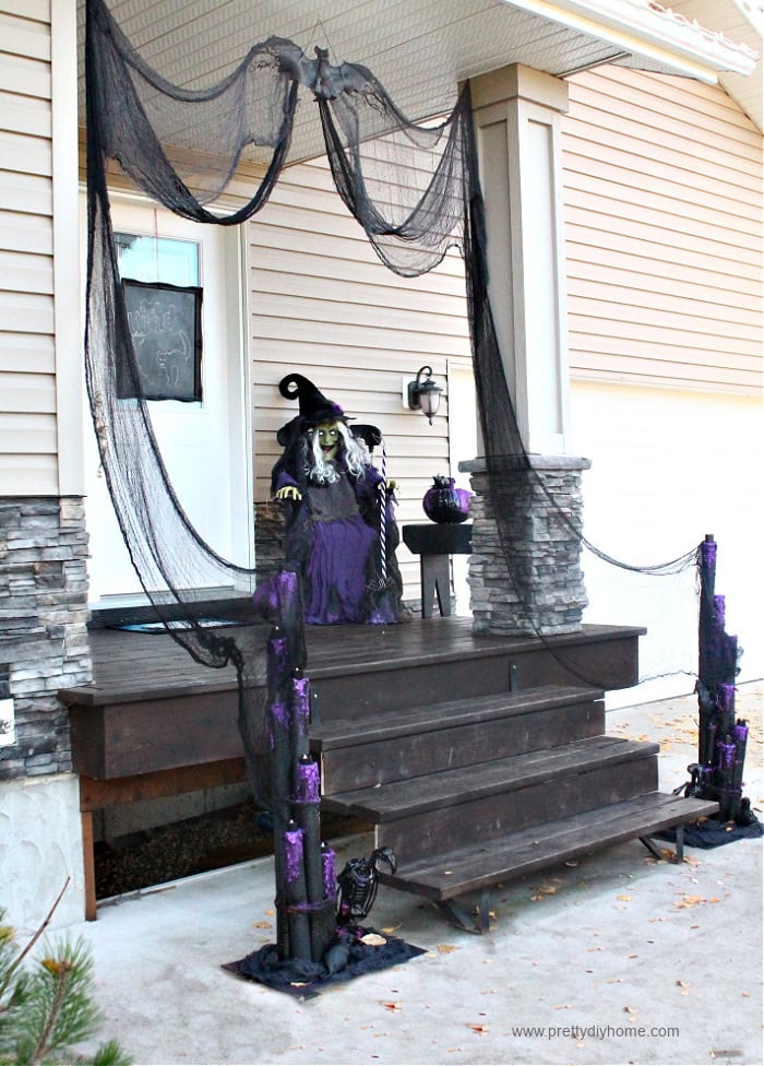 A scary Halloween front porch decorated with various scary DIY Halloween props including two large sets of pool noodle candles in black and purple with vultures, rats, black candles and spider.