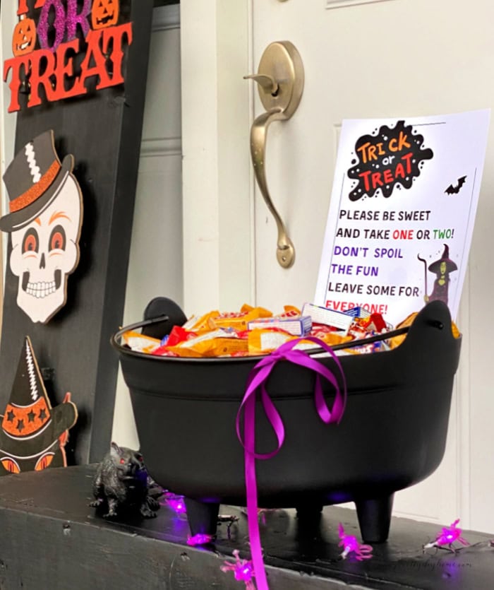 A Halloween candy sign set up on a Halloween porch with a cauldron full of various Halloween candy choices.