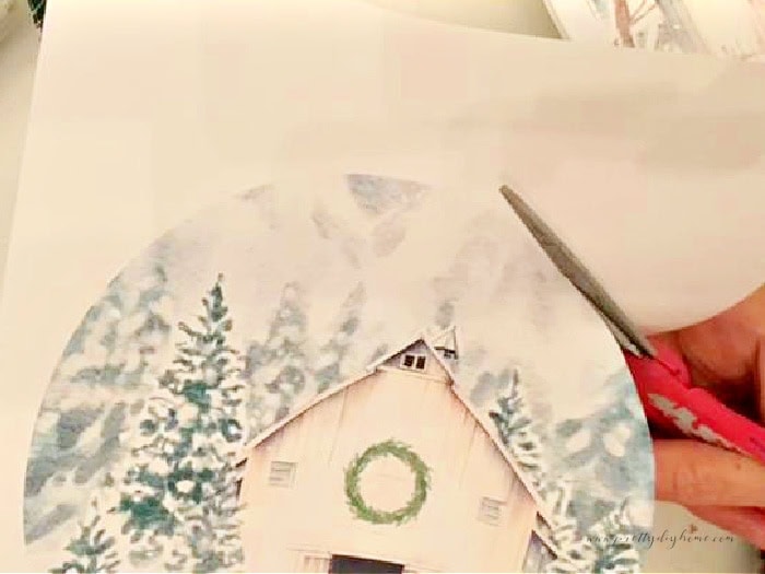 Cutting out a free printable white barn with snow covered trees. The printable is for making a dollar tree pie pan crafts for Christmas.