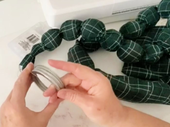 Adding small clear elastics to a jam jar lid prior to placing them on a fabric Christmas garland.