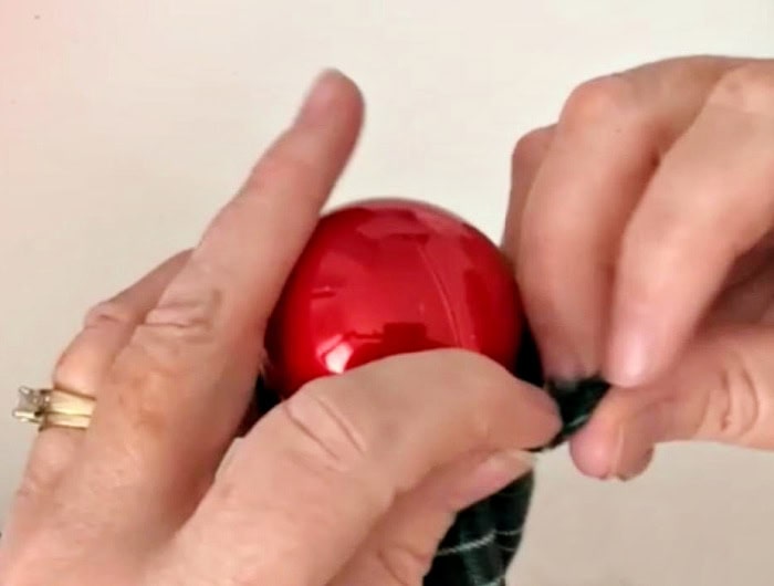 Adding a red Christmas ball inside a fabric tube, for filling a DIY Christmas garland craft made with Dollar Tree Christmas balls and fabric.