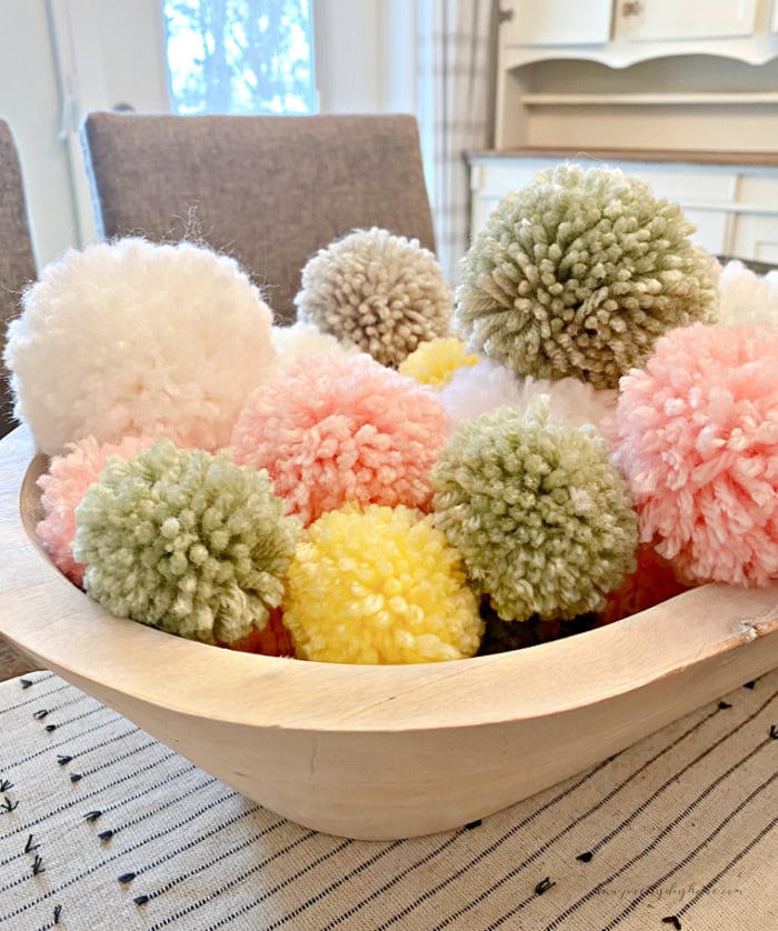 A large wool bowl filled to overflowing with various colored DIY Pom Poms made with a Clover Pom Pom Maker.