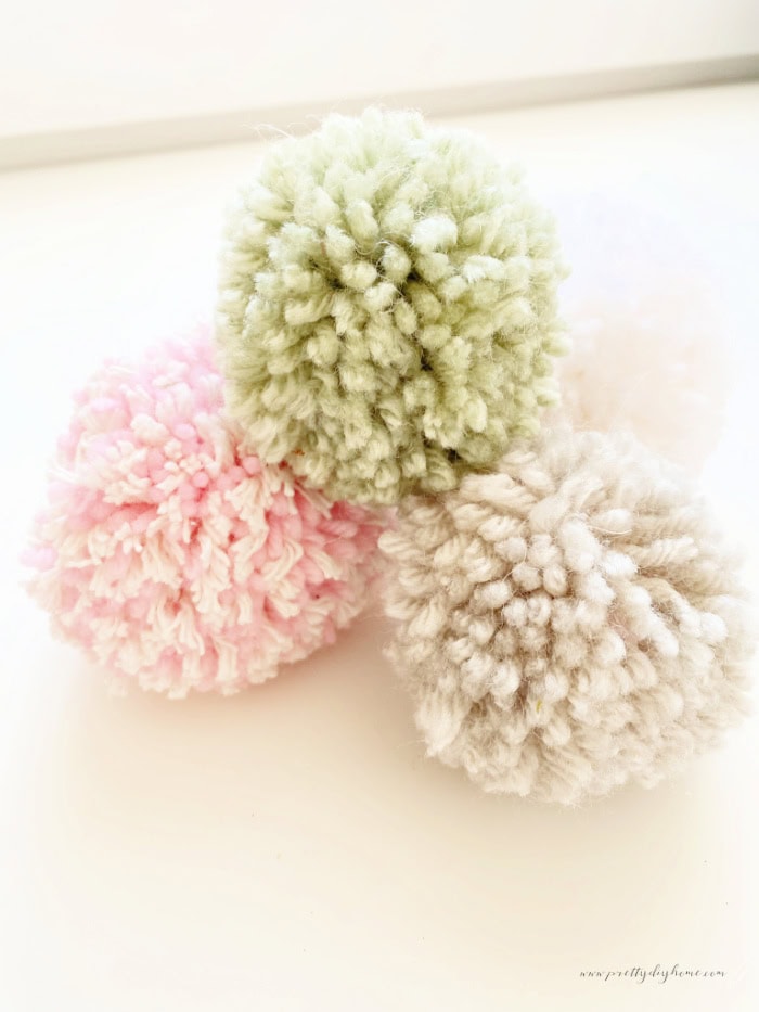 A small stack of pom poms made with cardboard in various colors, pink, grey, green and yellow.