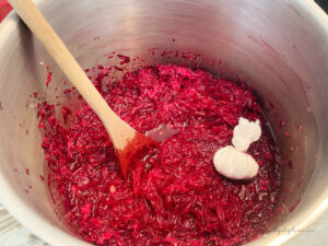 A large pot filled with the ingredients for beet and horseradish relish. You can see a cheesecloth bundle of pickling spice added.