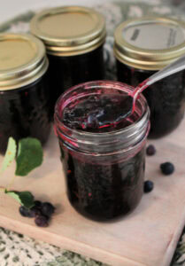 Four jars of homemade saskatoon jelly or service berry jam. There are four jars of the homemade jam on a cutting board.