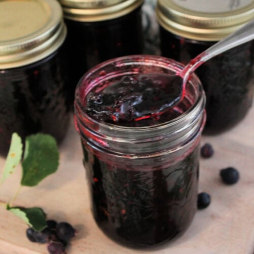 Four jars of homemade saskatoon jelly or service berry jam. There are four jars of the homemade jam on a cutting board.