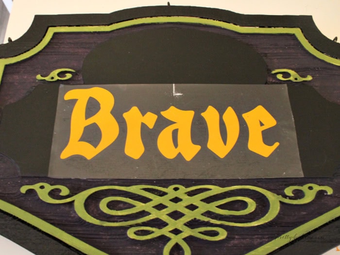 Orange “Brave” vinyl lettering applied to a painted black, green, and purple Halloween sign.
