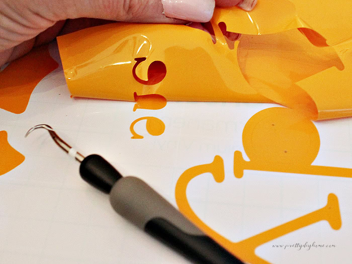Weeding orange vinyl lettering for a DIY outdoor Halloween sign.