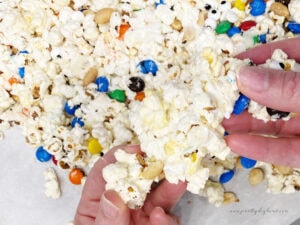 Breaking a slab of marshmallow covered Halloween popcorn into bite sized pieces. You can see the puffy marshmallows, M &Ms and peanuts in the candy.