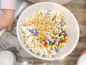 A large mixing bowl filled with popcorn, peanuts, M&Ms, and candy eyeballs for making Halloween popcorn.