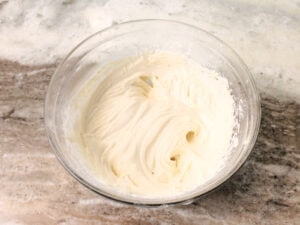 A clear glass bowl filled with light and cream sour cream glaze for placing onto a baked pumpkin bread.