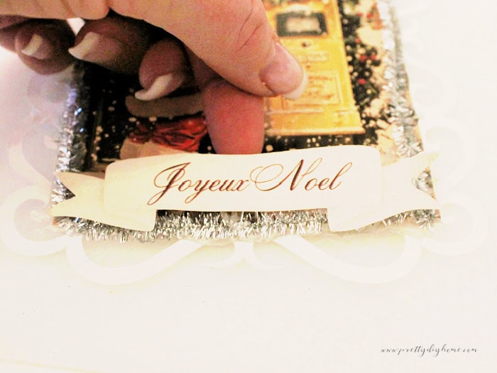 Lifting the ceneter of the Joyeux Noel ribbon banner to create a curved shape before gluing.