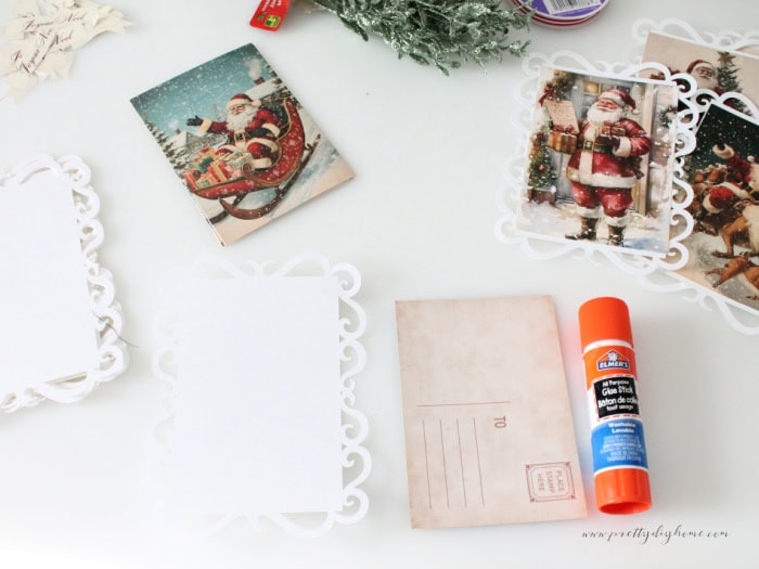 Supplies for making a DIY vintage Santa banner including postcards, a glue stick and cardstock lace backgrounds.