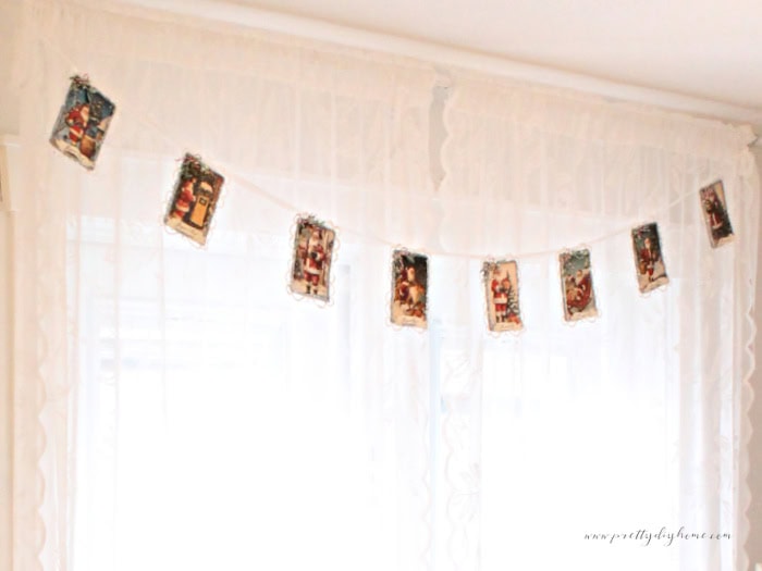 Vintage Santa banner displayed across the top of a lace-curtained window, cropped close for detail.