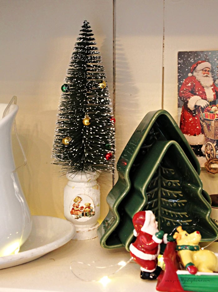 Close-up of a white spindle bottle brush tree displayed beside vintage ironstone dishes.