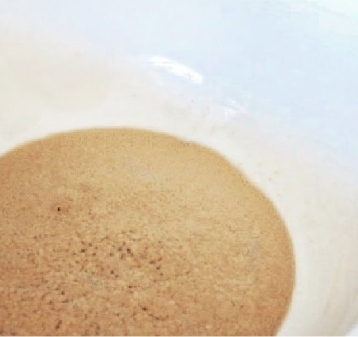 A close up of yeast in a small white bowl being softened for making hot cross buns.