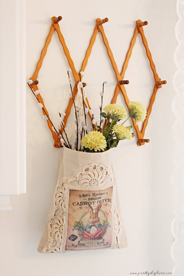 Linen bunny wall pocket hanging from a wooden accordion hanger as a DIY spring wreath alternative.