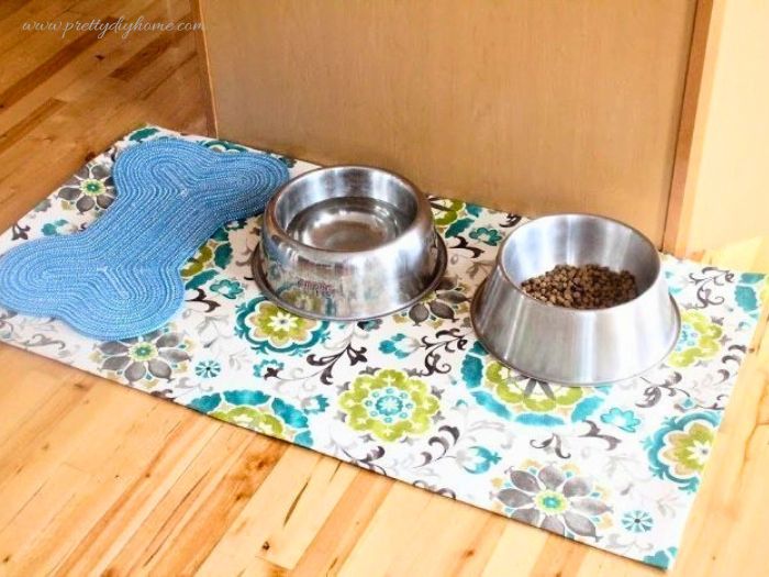 A large DIY pet feeding mat with stainless steel dog bowls and a blue bone placemat, protecting hardwood floors from spills.