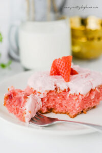 Close up of strawberry slab cake slice with cream cheese frosting and fresh strawberries.