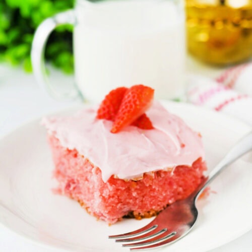 Slice of strawberry slab cake with cream cheese frosting topped with fresh strawberries on a plate with a fork and milk in the background.