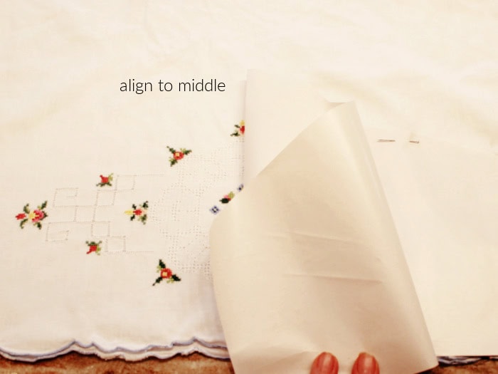 Aligning the center of the DIY hanger cover pattern with the embroidered design on a vintage pillowcase before cutting.