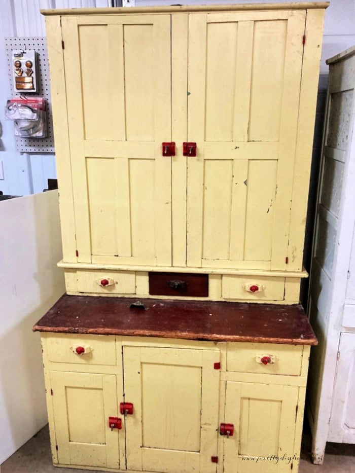 Original antique kitchen cabinet before makeover with yellow paint, vintage hardware, and dark wood countertop.
