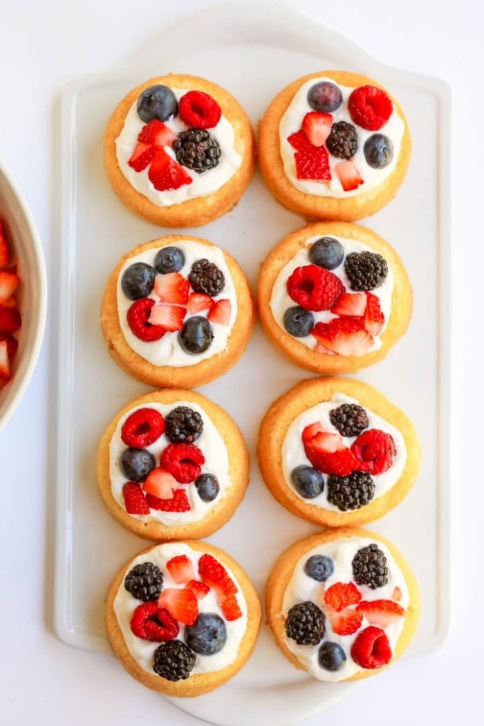 A tray of eight blueberry strawberry shortcakes topped with cheesecake whipped cream and fresh berries.