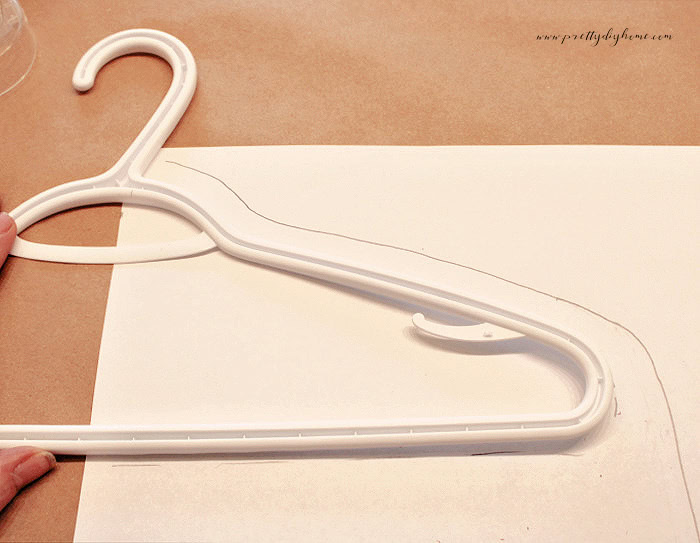 Tracing half of a DIY hanger cover pattern using a plastic clothes hanger as a template on folded paper.