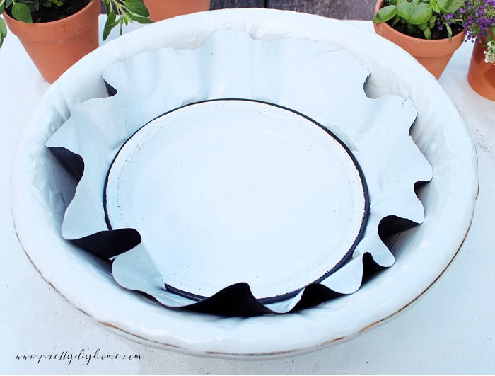Preparing a vintage porcelain wash basin for a container herb garden using plastic, garden fabric, and an enamel plate.
