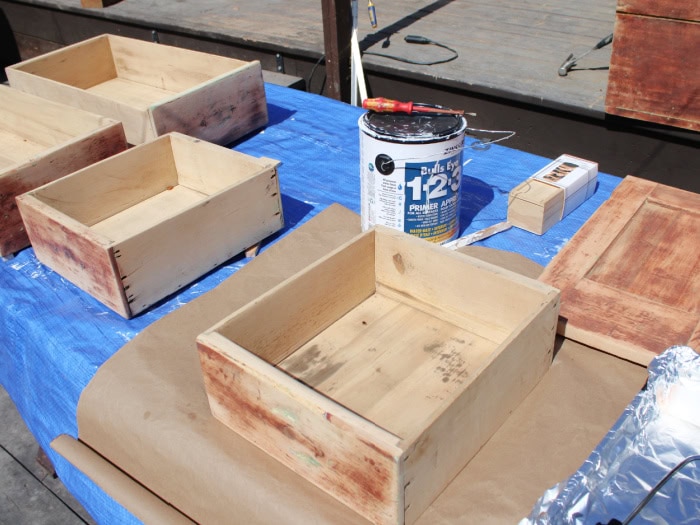 Priming vintage cabinet drawers before painting during an antique kitchen cabinet makeover project.
