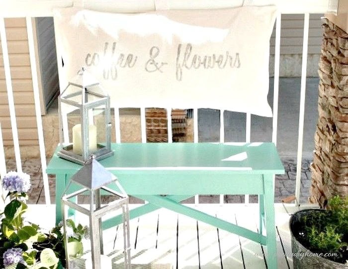 Small front porch seating with a DIY bench and cushion back creating a simple and comfortable outdoor spot.