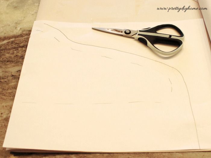 The folded paper DIY hanger cover pattern with the seam allowance added before cutting out the symmetrical shape.