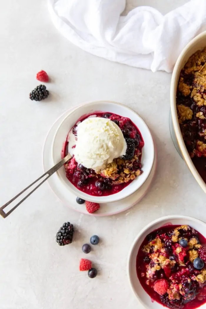 Triple berry crisp topped with vanilla ice cream and fresh berries