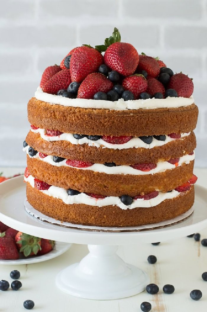 Four layer vanilla naked cake filled with fresh strawberries, blueberries, and creamy frosting.