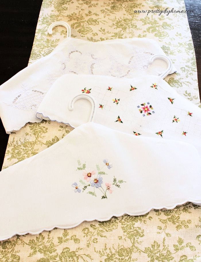 Several repurposed vintage linen hanger covers made from embroidered pillowcases displayed together on white hangers.