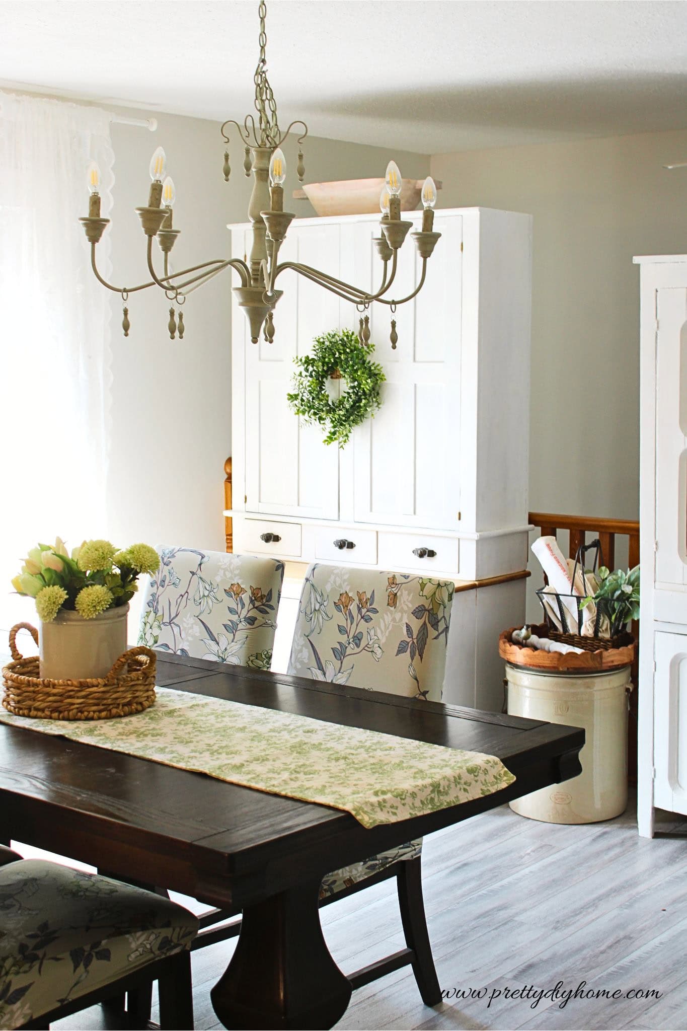 Vintage white kitchen cabinet styled in a cozy dining room with cottage decor, antique furniture, and warm neutral accents.