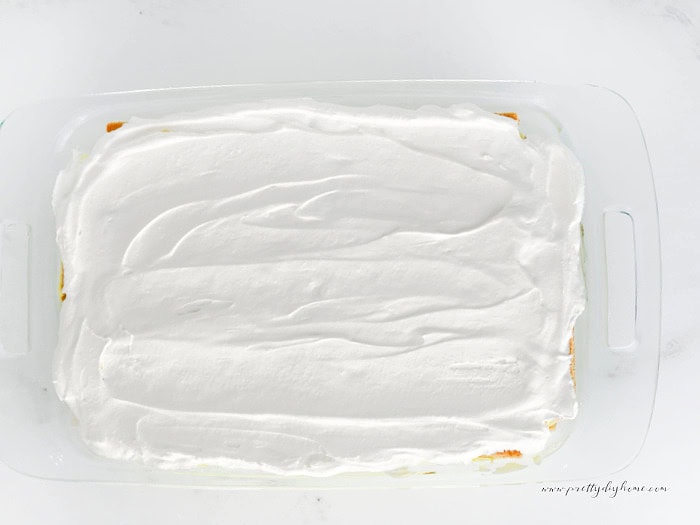 Fresh whipped cream spread over the top of a lemon icebox cake in a clear glass baking dish.
