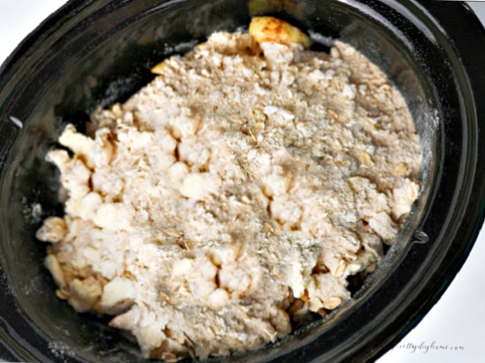 Apple crisp ready for cooking in a slow cooker with cinnamon coated apples covered by a homemade oat crumble topping.