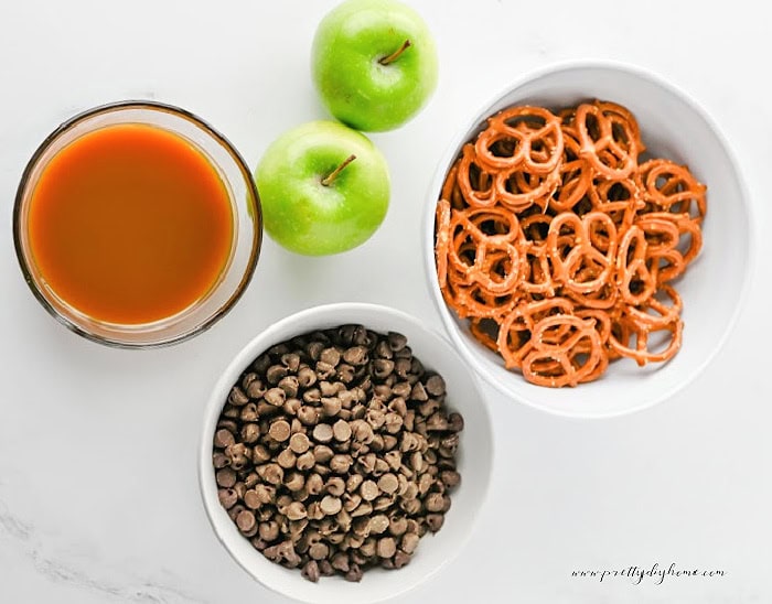Ingredients for caramel apple bark including Granny Smith apples, chocolate chips, pretzels, caramel sauce, and lime juice.