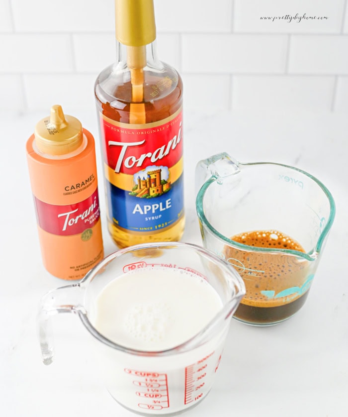 Ingredients for making a caramel apple latte including milk, espresso, apple syrup, and caramel syrup.