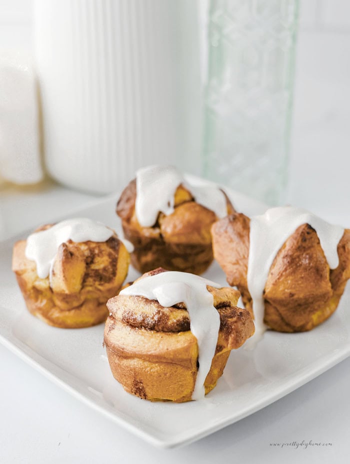 Cinnamon roll muffins arranged on a white serving plate with a drizzle of icing.