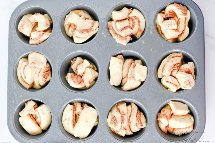Cut cinnamon roll pieces arranged in a greased muffin tin before baking.