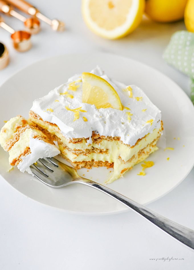 A slice of creamy lemon icebox cake with a bite removed, showing layers of lemon filling, graham crackers, and whipped cream topping.