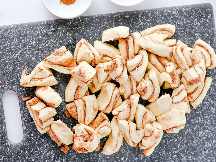Cut cinnamon roll dough pieces on a cutting board for making cinnamon roll muffins.