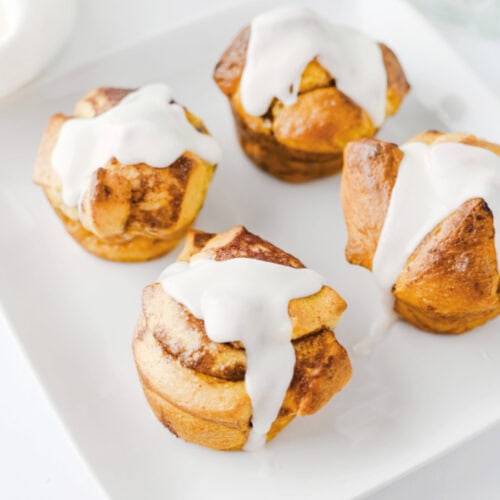 Easy cinnamon roll muffins topped with sweet icing and served on a white plate.