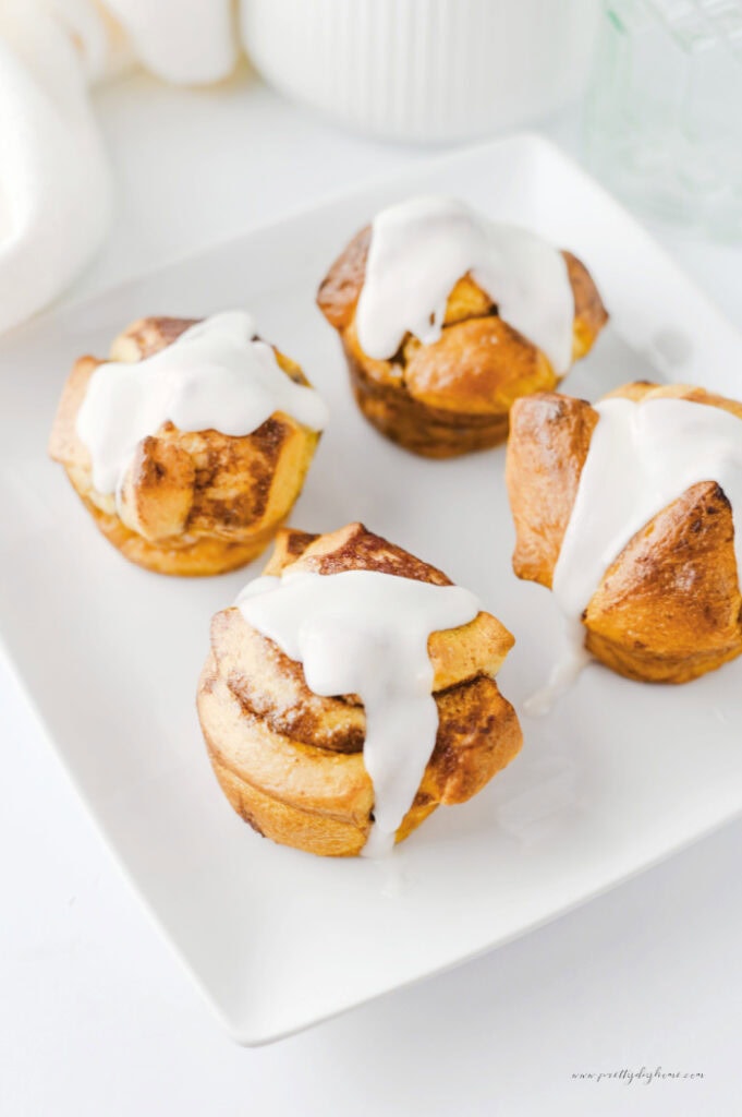 Easy cinnamon roll muffins topped with sweet icing and served on a white plate.