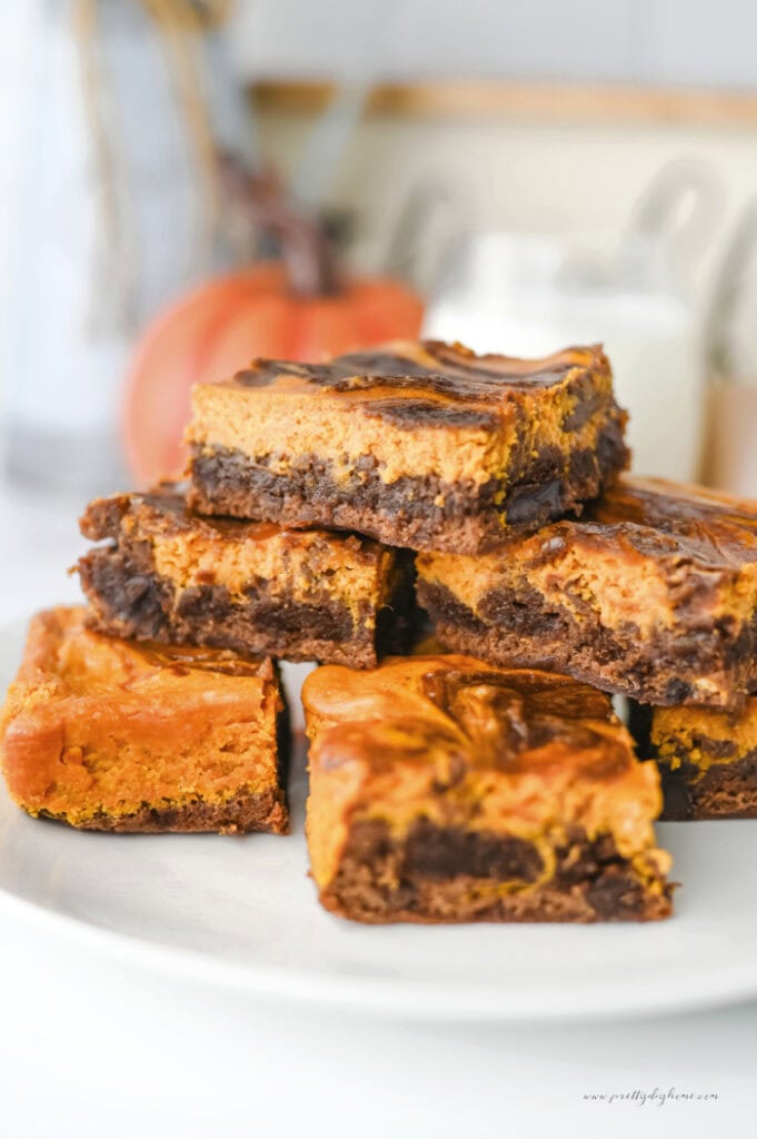 Easy pumpkin brownies with a creamy pumpkin cream cheese swirl and rich chocolate chips stacked on a white plate.